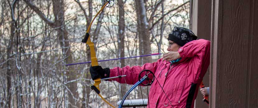 A woman pulls back a bow at the archery range.