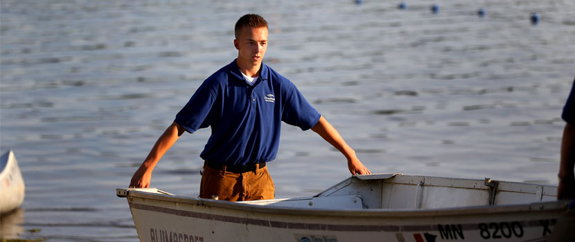 A man wearing a shirt with a Three Rivers Park District logo holds a boat in water.