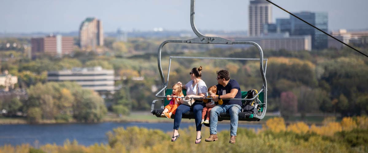 A family rides in a chairlift at Hyland Hills, looking across the lake.