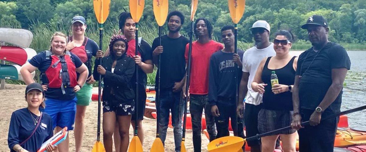 A group of people stand with kayak paddles stand on the shore at an event put on by Innovative SOULutions and Three Rivers Park District.