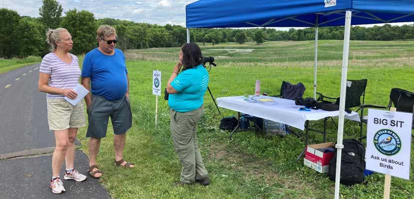 Photo of a Three Rivers staff member standing on grass near a tent, talking to visitors at Baker Park Reserve on the day of the Big Sit.