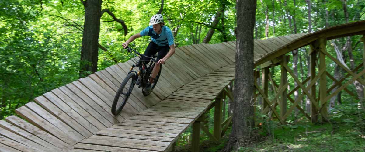 A mountain biker rides down a new wooden bridge feature on the Monarch Singletrack at Carver Park Reserve.