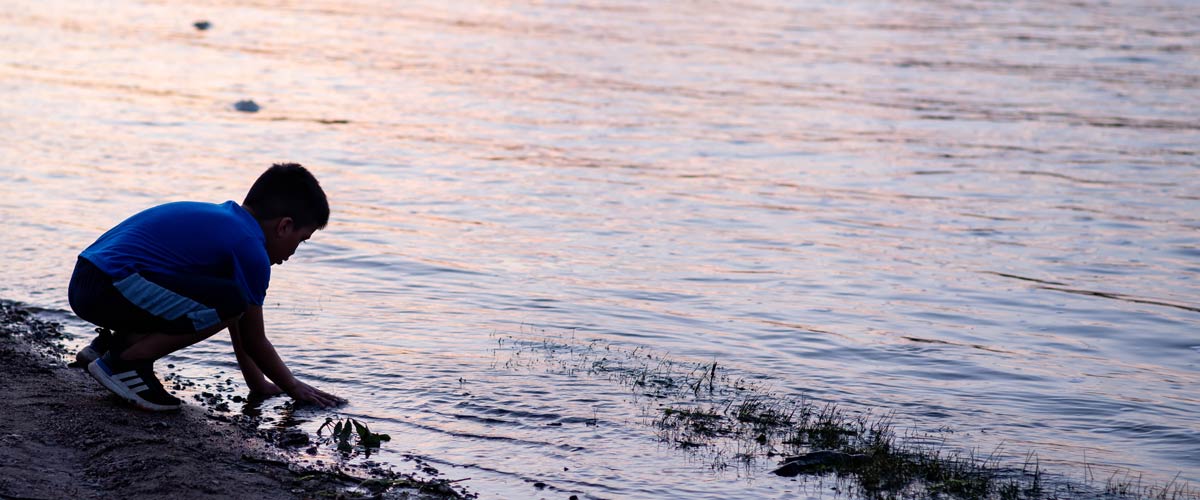 A photo of a child putting his hands in the water on the shore of the Mississippi River