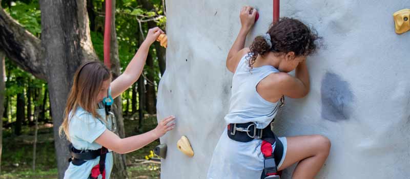 Two Girl Scouts climb the climbing wall at Baker Outdoor Learning Center.