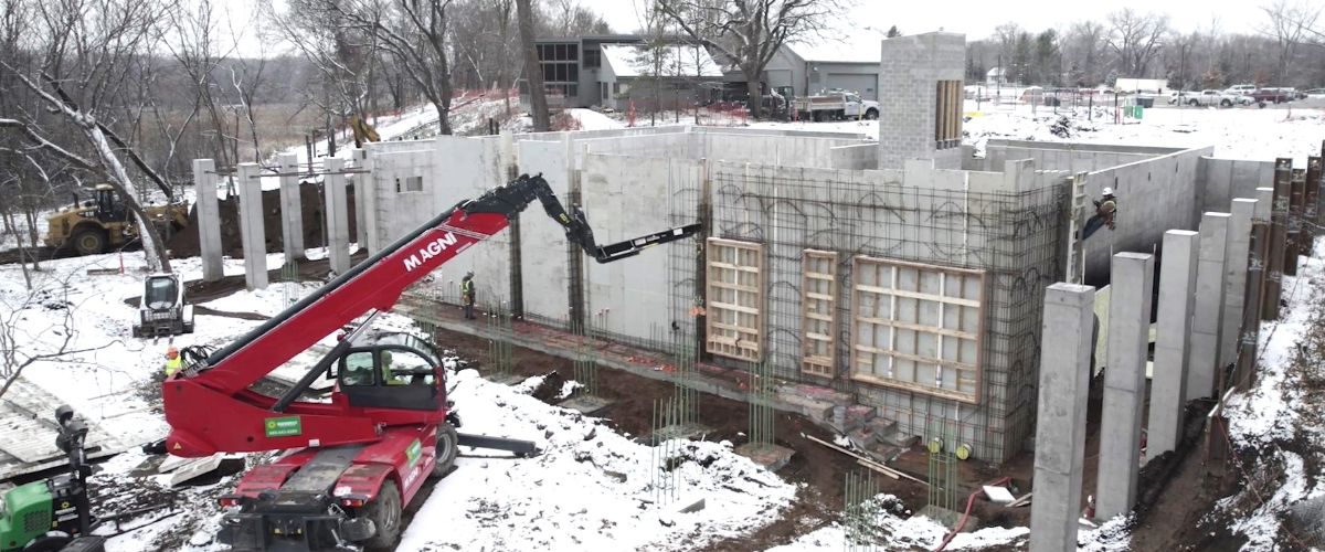 a concrete building foundation with snow on the ground and a red construction crane