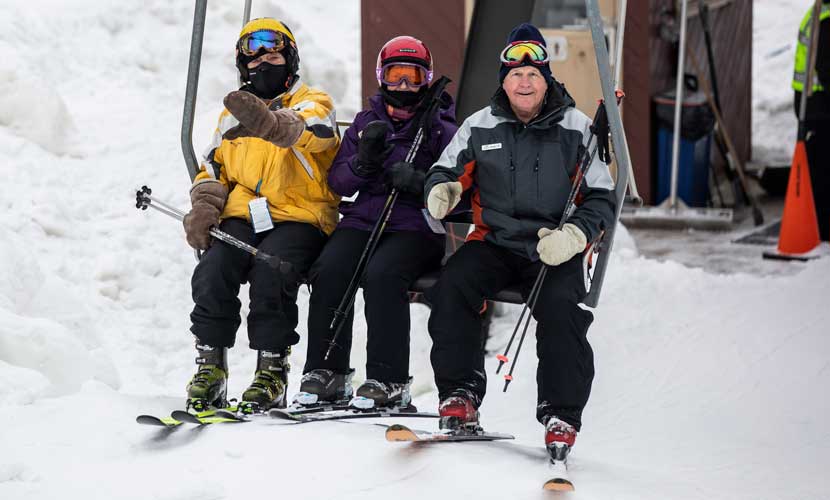 Three skiers sit on a chairlift.