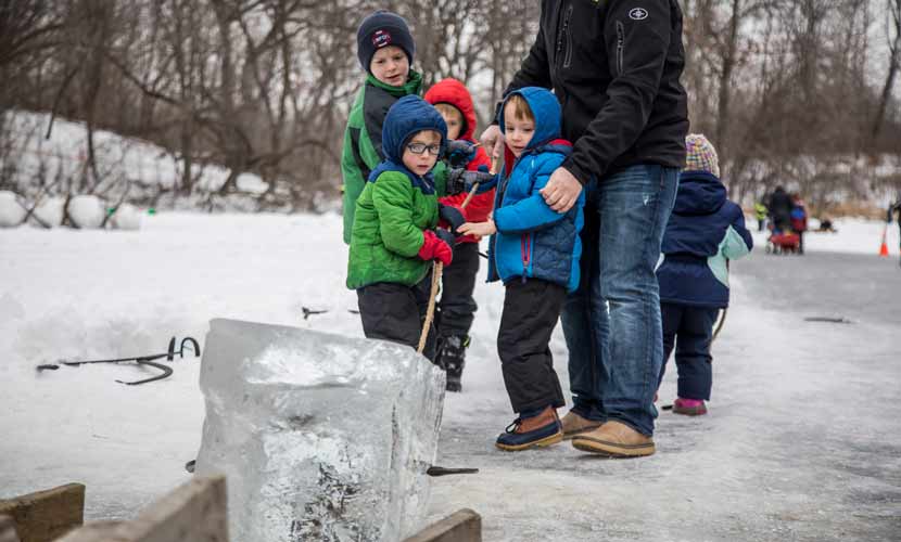 Four kids hold onto a rope and pull a cube of ice off of a chute and out of the lake.