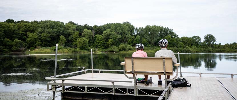 Two bikers rest on a bench overlooking wetlands in Carver Park Reserve.