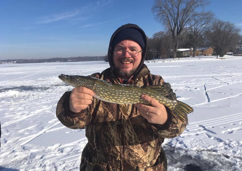 A man smiles as he holds up a fish he caught while ice fishing.