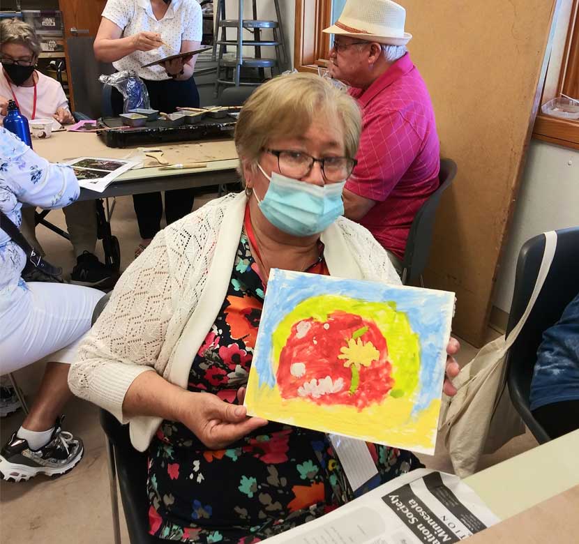 A woman wearing a mask holds up a painting she completed at Silverwood Park in St. Anthony.