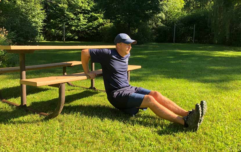 A man demonstrates using a picnic table for tricep dips. 