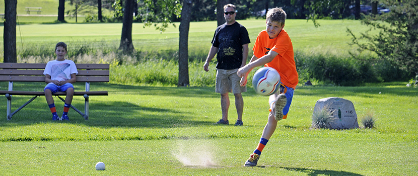 A boy kicks a soccer ball on a golfing green