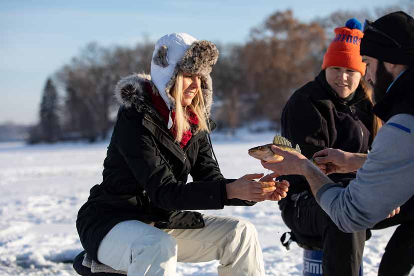 A woman is handed a fish caught from ice fishing.