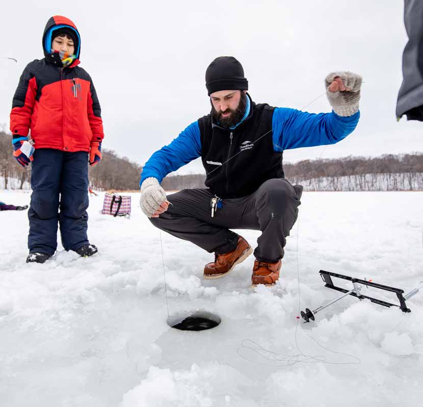 Three Rivers Recreation Program Specialist Nick Sacco sets up a tip-up at a hole in the ice as a child watches.