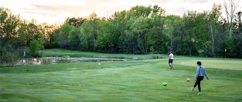A man and a woman play footgolf during sunset at Baker National Golf Course.