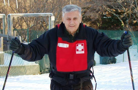 man in a red park patrol vest with ski poles in his hand