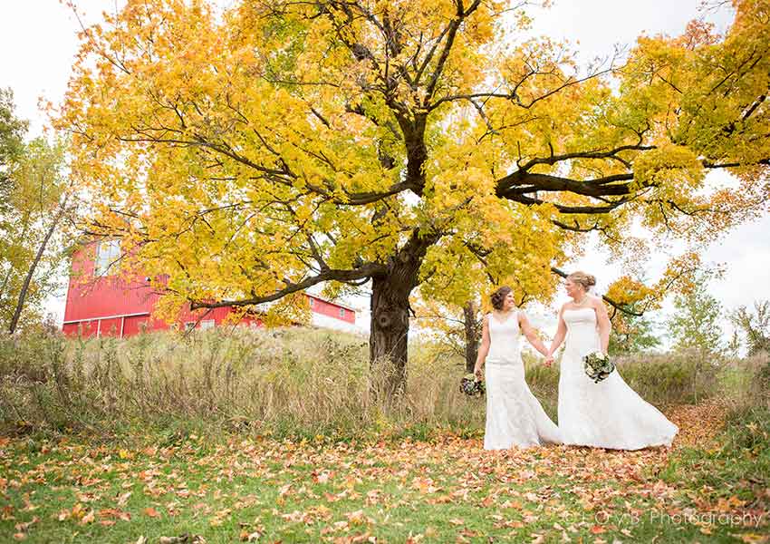 brides walking a fall trail with a red barn in the background