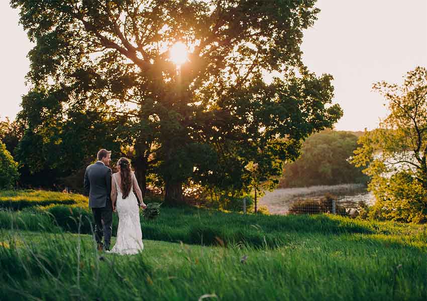 bride and groom outside by a large oak tree at sunset with Whaletail Lake in the background