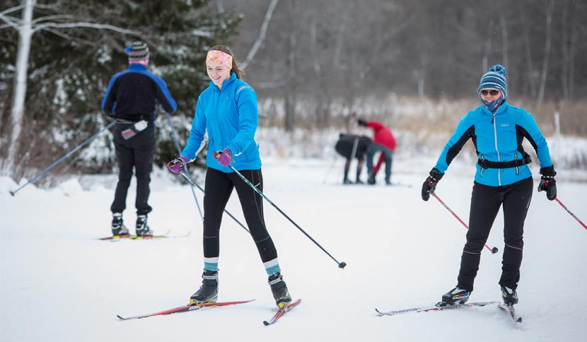 two women in blue jackets smiling while cross-country skiing.