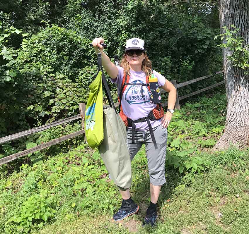A woman in a trucker hat holds up a bag of trash collected from the trail.