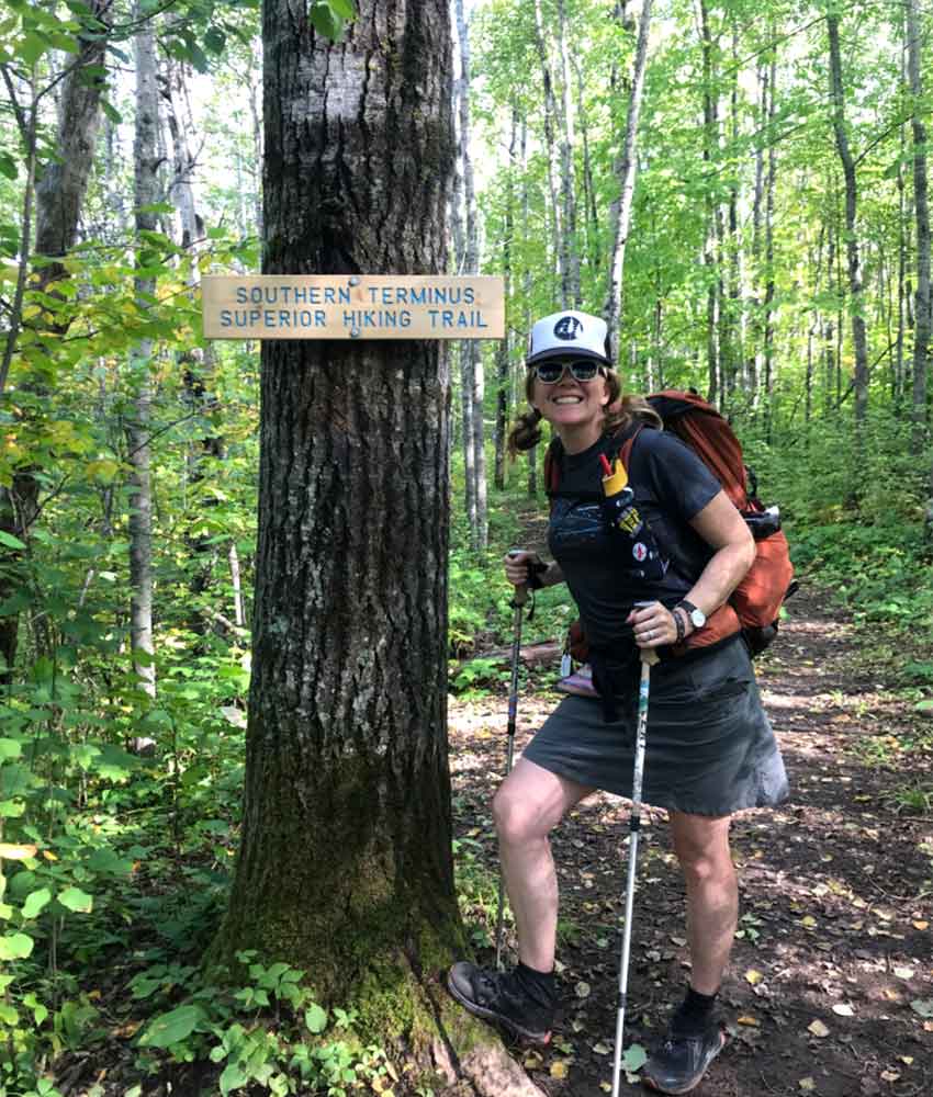 A woman hiker stands next to a superior trail hiking sign.