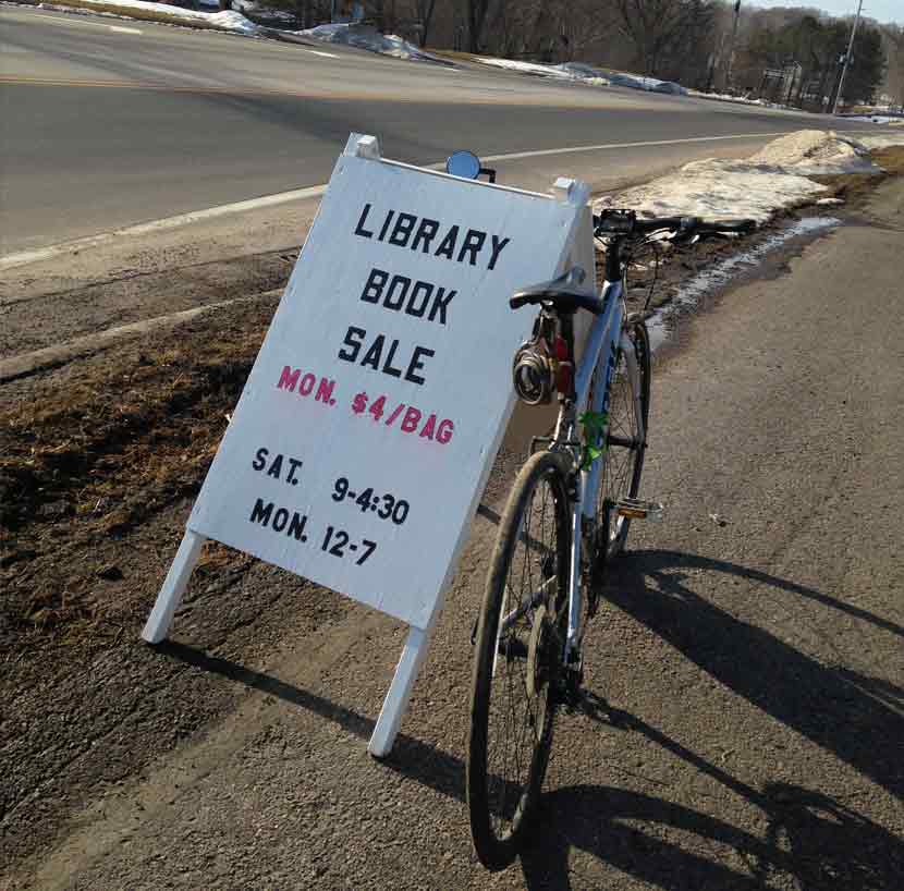 A bike parked next to a library sandwich board sign.