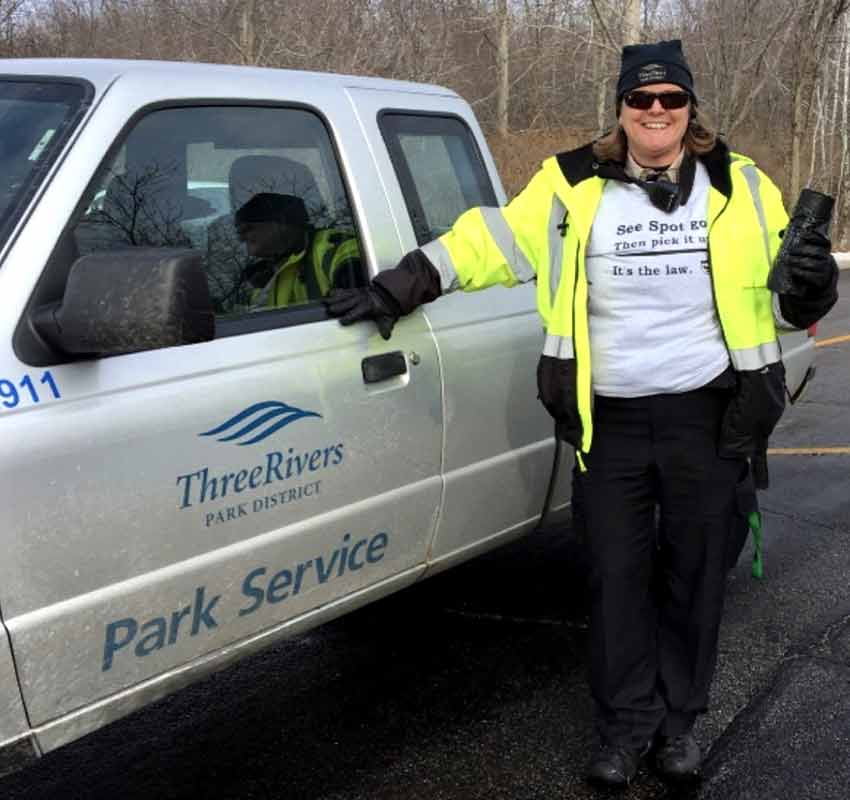 Lori in uniform standing next to a gray Three Rivers truck that says "Park Service."
