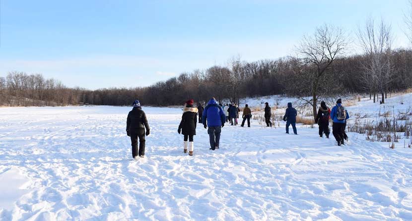 group of people dressed in winter gear walking on a snow-covered pond in the woods
