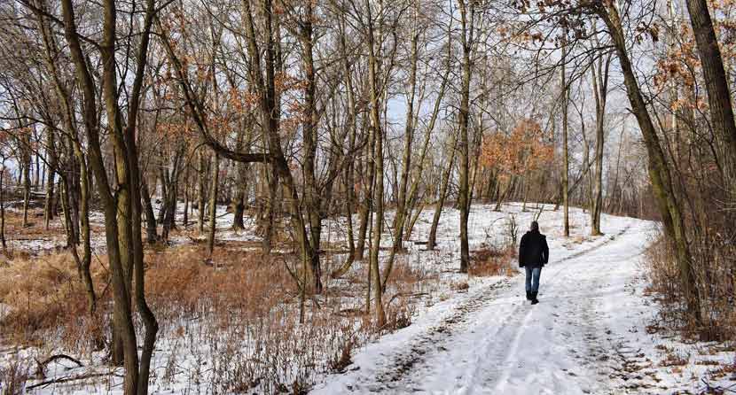 man hiking on a snowy trail through the woods