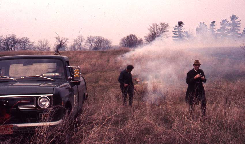 two men in a prairie doing a prescribed prairie burn in the 1970s
