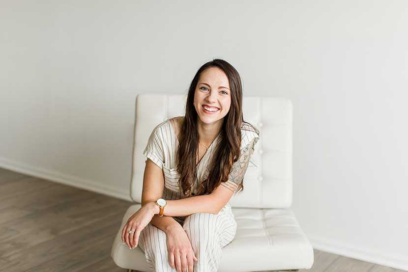 A photo of a woman sitting on a white chair smiling.