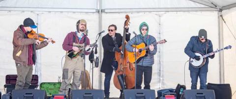 Photo of a band playing on stage, dressed in winter outerwear.